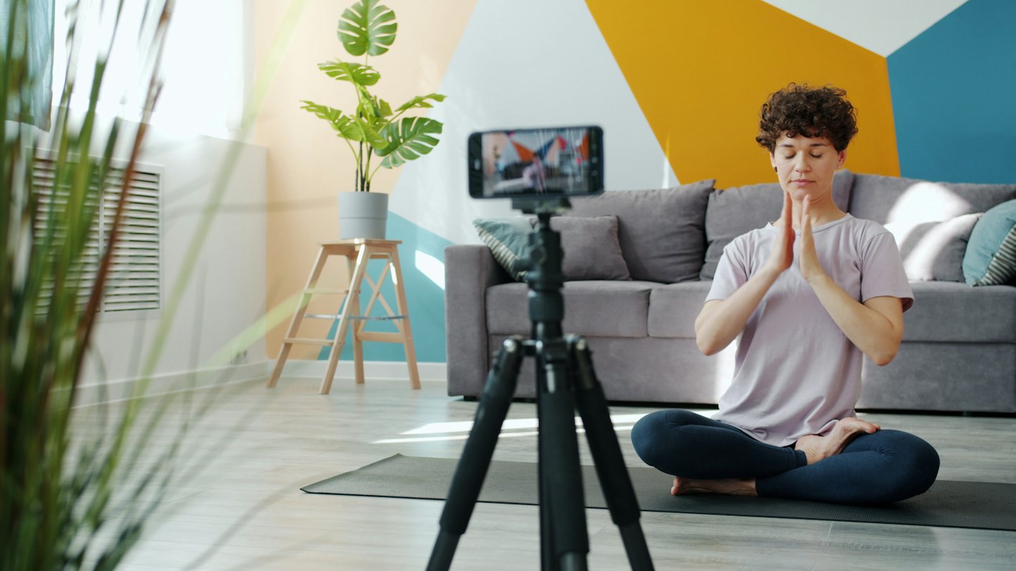 Mujer meditando en un salón moderno grabando su sesión.